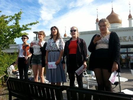 Fem kvinnor ställer sig upp och sjunger en sång om kvinnors rättigheter
