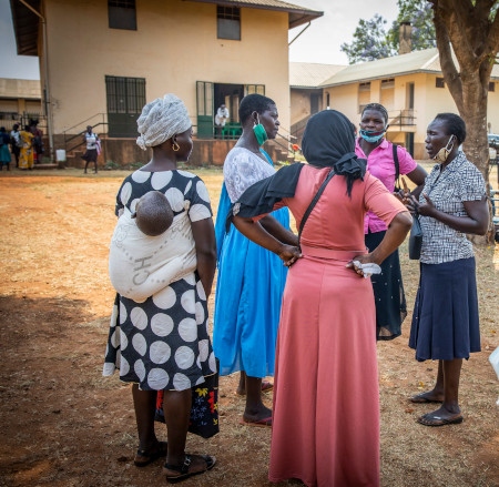 Några kvinnor står och pratar utanför St. Monicas skola i Gulu efter rättegången mot Ongwen. Många är upprörda över att Ongwen straffas för handlingar han blev tvingad att utföra. Grace Adong (i blå klänning) är en av dem. 