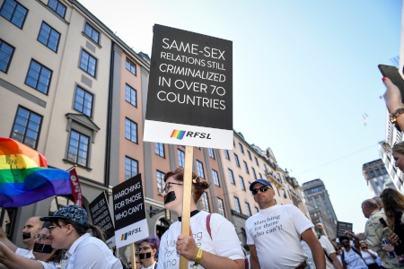 Deltagare från RFSL i Prideparaden i Stockholm 2019 med en skylt som påminner om att samkönade relationer fortfarande är kriminaliserat i över 70 länder.